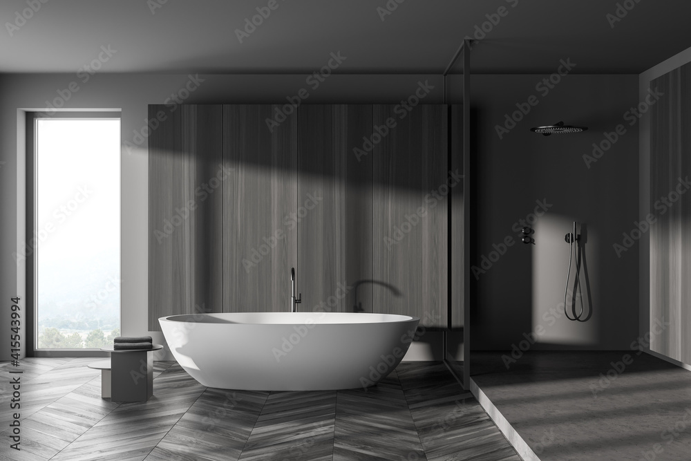 Interior of modern bathroom with grey wooden walls, concrete floor, comfortable white bathtub and shower cabin.