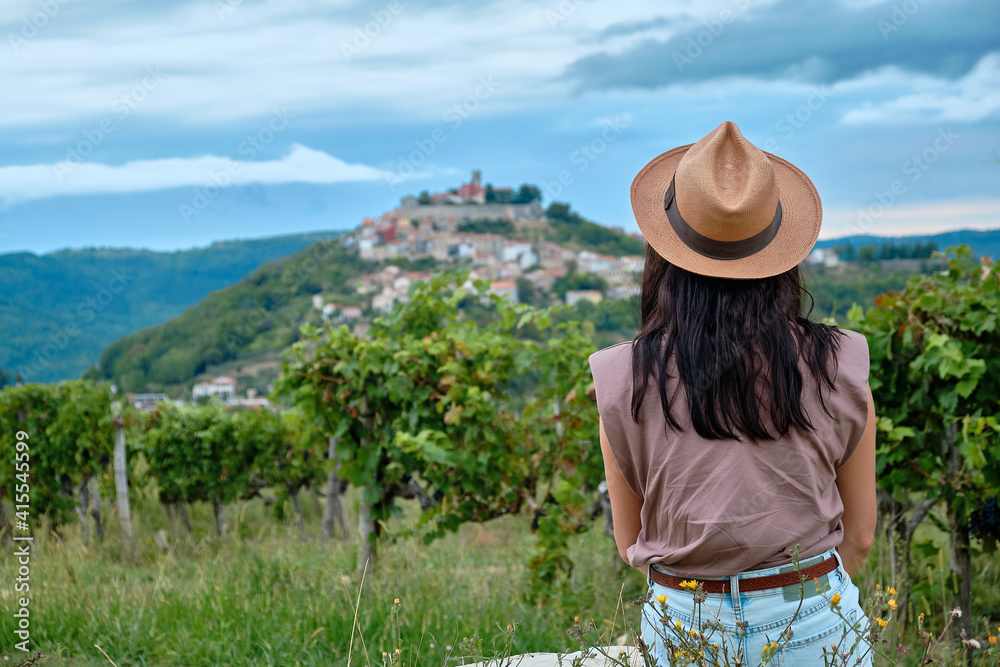 Motovun, Croatia. Girl in a straw hat siting in vineyards with view of Motovun in Croatia. 