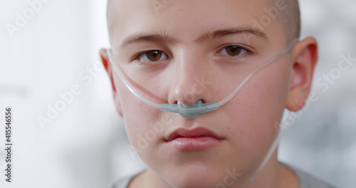 Close up portrait of sad sick boy with nasal cannula looking at camera in hospital photo