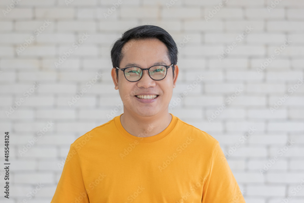 Obraz premium Portrait of adult Asian man wearing yellow t-shirt and eyeglasses standing and smiling looking to camera with friendly and self confident