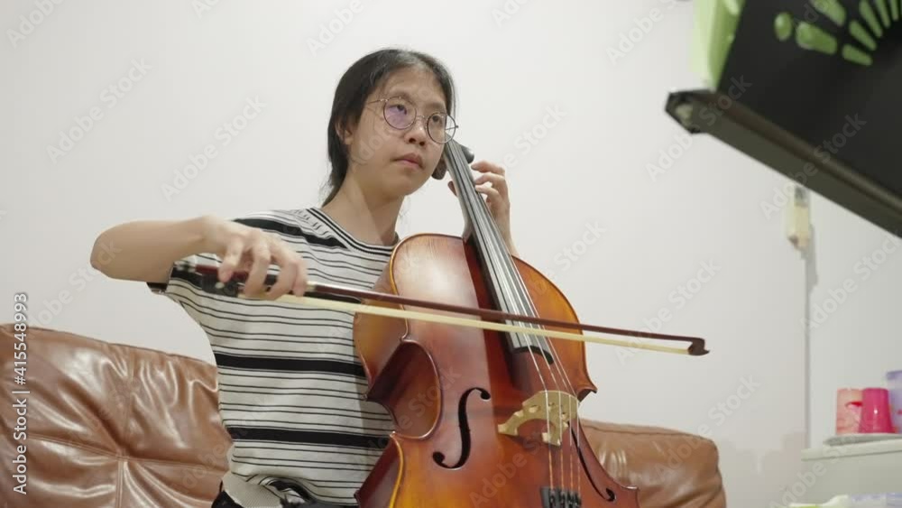 Young happy Asian female teenager practicing her cello at home, filmed in slow motion Young happy Asian female teenager practicing her cello at home, filmed in slow motion
