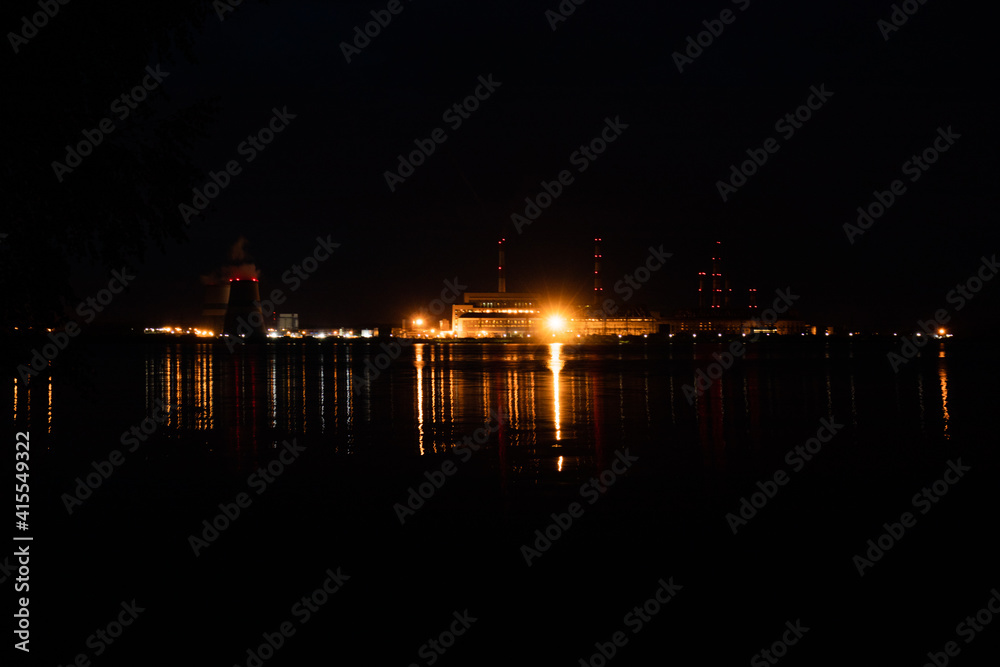 View of the thermal power plant from the bank of the reservoir at night. A lot of backlighting in different colors.