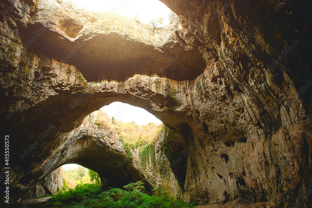 Devetashka cave in Bulgaria - natural attraction. High arches of a huge stone cave with round holes at the top, a tourist road with a fence inside the cave. 