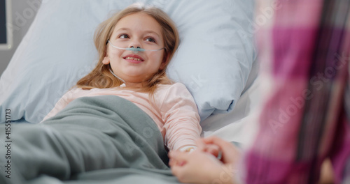 Cute preteen girl lying in hospital bed and holding mother hand