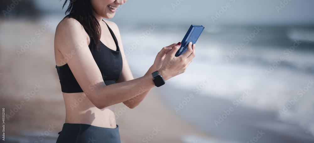 Wellbeing athlete sport concept, Asian muscular healthy woman jogging running looking at smartphone on beach