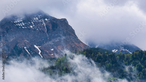 A forest and Mount Pilatus with little snow on the rocks are crossed by clouds of fog 