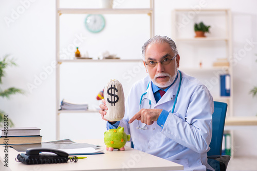 Old male doctor holding moneybag in the hospital