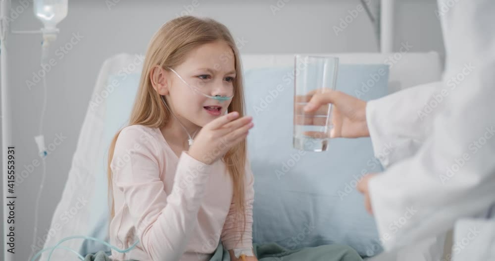 Sick little girl taking pill and glass of water from doctor sitting in hospital bed Sick little girl taking pill and glass of water from doctor sitting in hospital bed