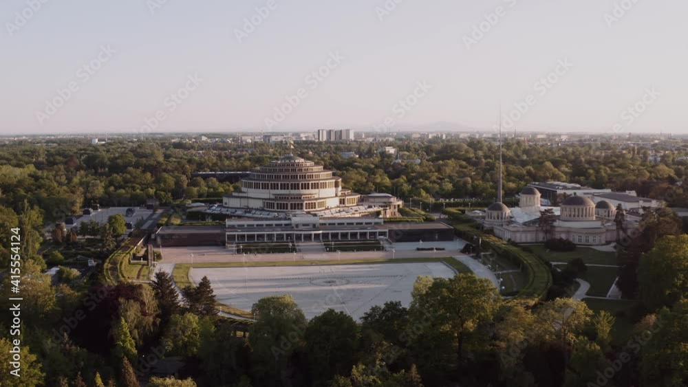 Aerial shot of a beautiful park with large, modern building in the middle. Round, huge architecture in a green city. Urban landscape drone shot.