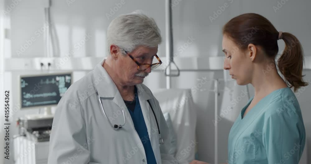 Worried mother talking to aged oncologist with sick boy resting in bed