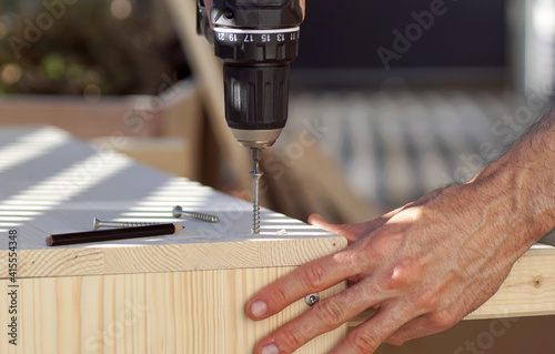 Close up a hand using a screwdriver while building a wooden raised bed in spring