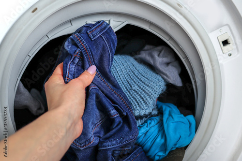 Female hand getting out clean jeans clothes from a washing machine at home