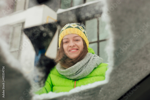 Girl with emotional face cleaning the windshield of a car from snow.