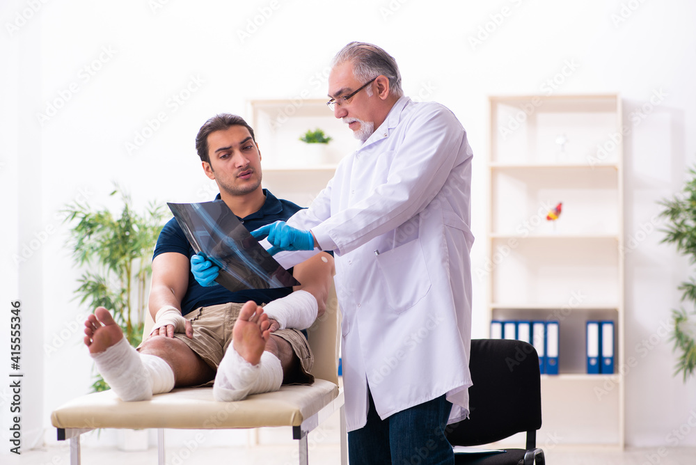 Young injured man visiting old doctor traumatologist Young injured man visiting old doctor traumatologist