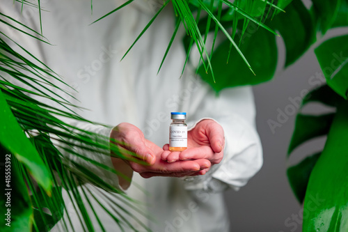 Fototapeta Naklejka Na Ścianę i Meble -  Woman in white shirt show vaccine in a bottle near palm leaves.