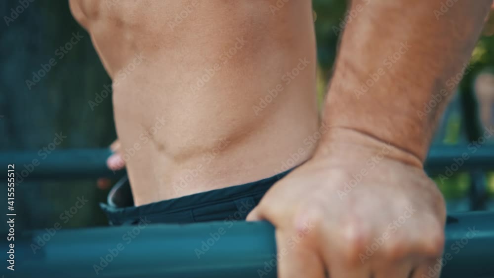 Close-up of athletic man doing hard intense exercises pull ups on parallel bars. Sportsman practicing training workout outdoors. Close-up of athletic man doing hard intense exercises pull ups on parallel bars. Sportsman practicing training workout outdoors.