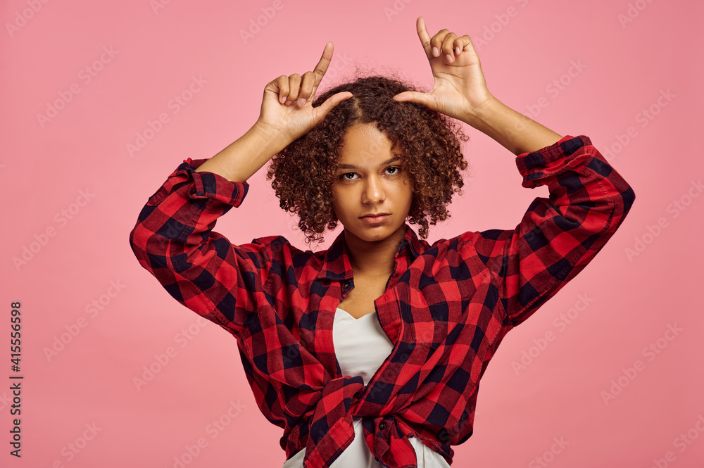 Young woman shows horns, pink background, emotion Young woman shows horns, pink background, emotion