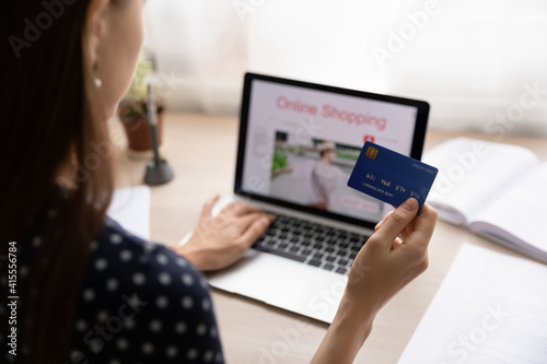 Close up back view of woman sit at desk pay with credit card shopping online on laptop from home. Female buyer or client use secure internet banking service system, make payment on web on computer.