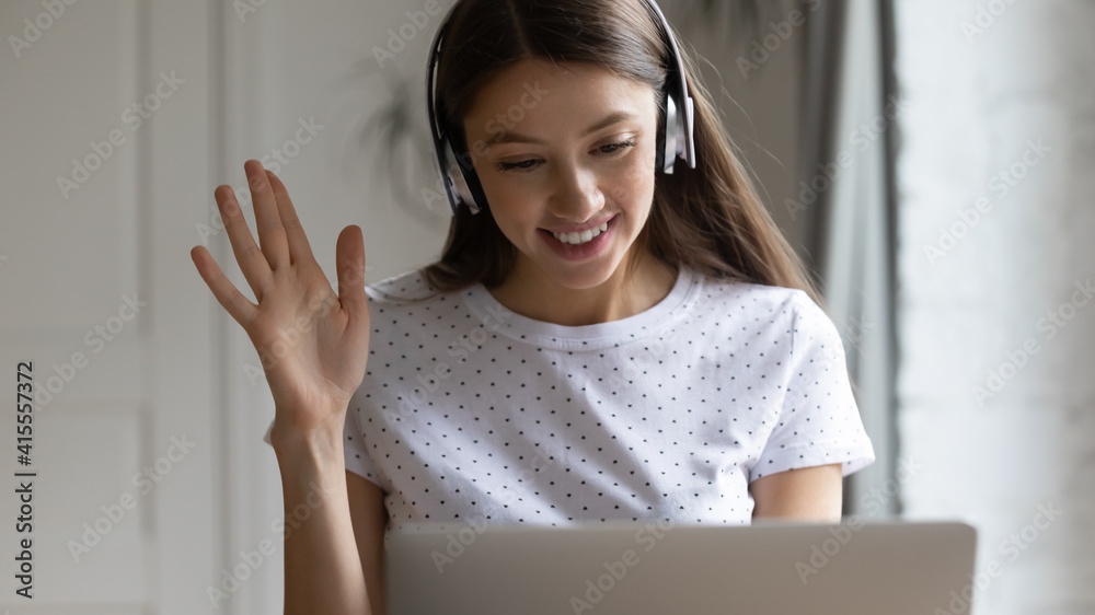 Wide banner close up view of smiling millennial Caucasian woman in headphones wave greeting talking on video call on laptop. Happy young female earphones have webcam digital virtual conference online. Wide banner close up view of smiling millennial Caucasian woman in headphones wave greeting talking on video call on laptop. Happy young female earphones have webcam digital virtual conference online.