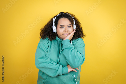 Young african american girl wearing gym clothes and using headphones thinking looking tired and bored with crossed arms © Irene