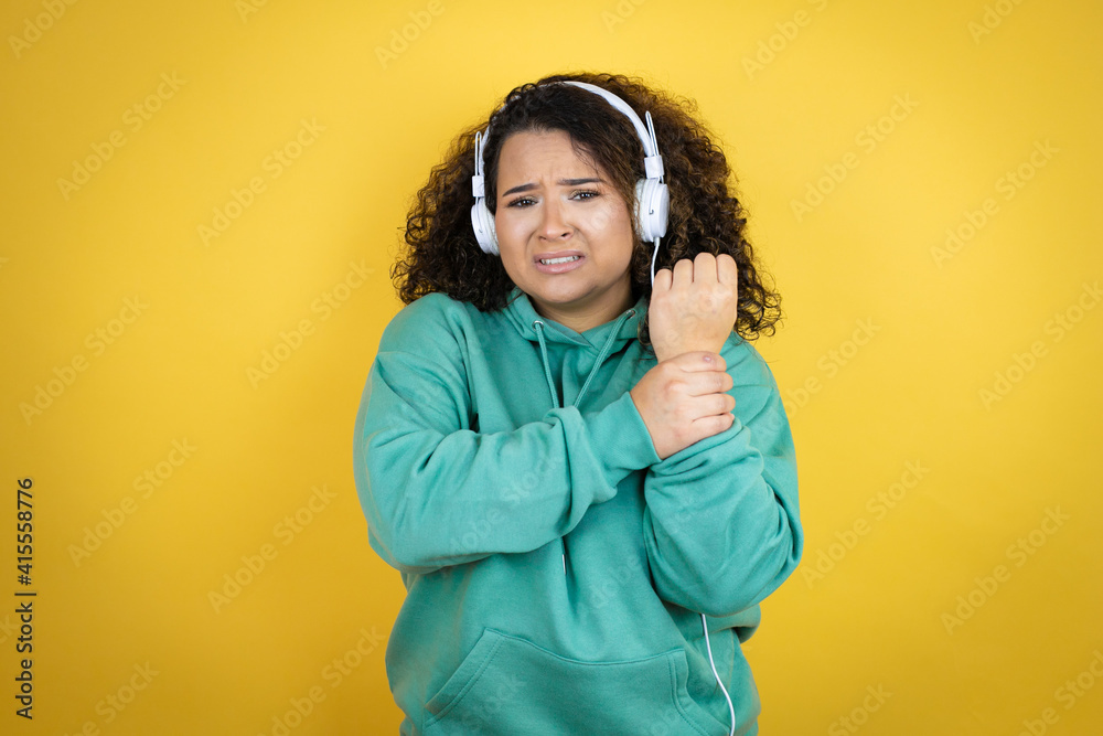 Young african american girl wearing gym clothes and using headphones suffering pain on hands and fingers, arthritis inflammation Young african american girl wearing gym clothes and using headphones suffering pain on hands and fingers, arthritis inflammation