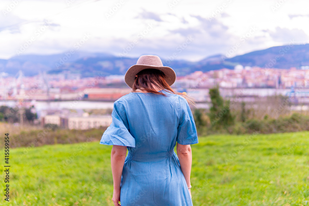 Beautiful young middle-aged woman looking at the landscape in spring with blue dress and hat.