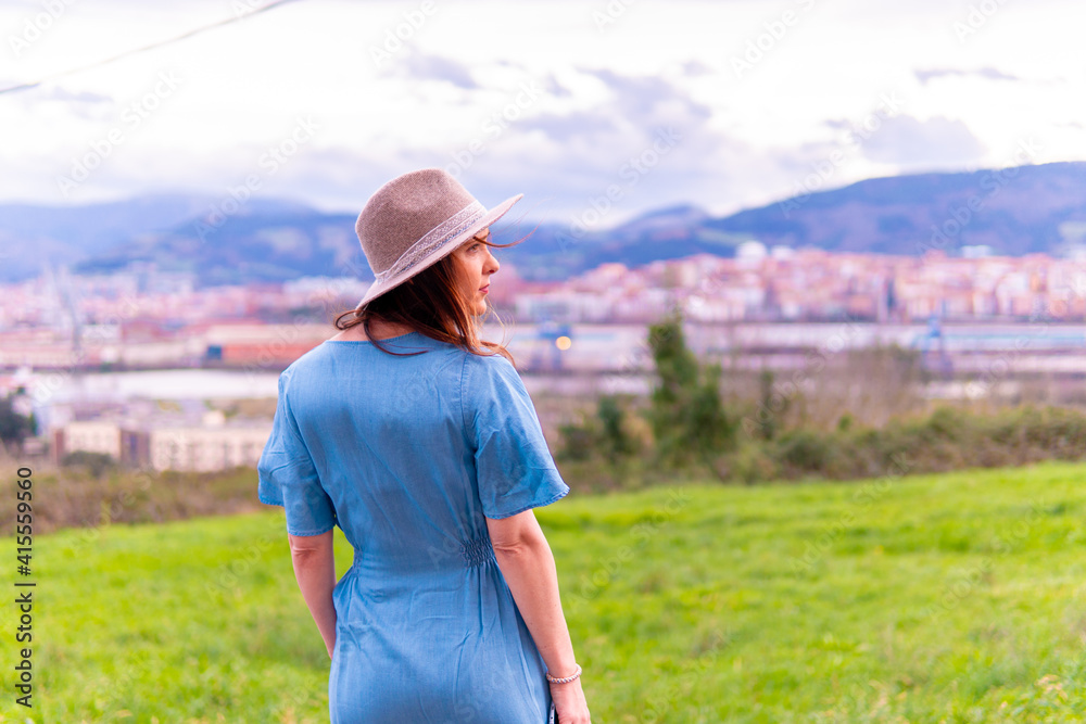Beautiful young middle-aged woman looking at the landscape in spring with blue dress and hat.