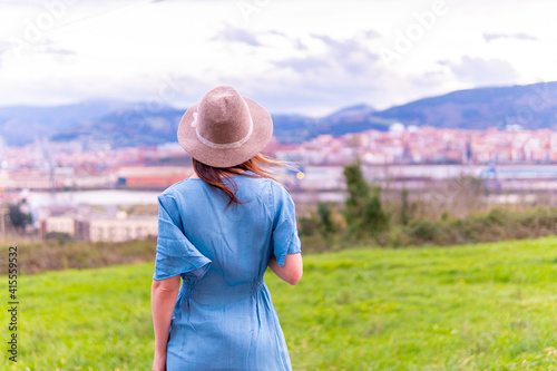 Beautiful young middle-aged woman looking at the landscape in spring with blue dress and hat.