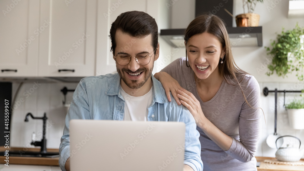 Wide banner panorama view of smiling millennial Caucasian man and woman look at laptop screen win lottery online. Happy young couple feel overjoyed read good news or amazing discount deal on computer.