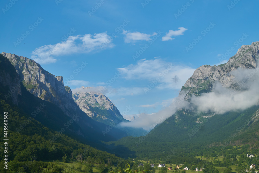 View on beautiful valley in Montenegro with mountains, clouds, blue sky, forests and some houses