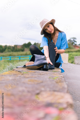Middle-aged young beautiful woman in blue dress hat and high leather boots removed with sore feet in a countryside area massaging her feet. fashion concept