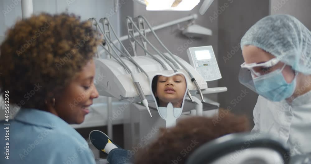 African little girl sitting in dental chair and looking in mirror visiting dentist with mother African little girl sitting in dental chair and looking in mirror visiting dentist with mother