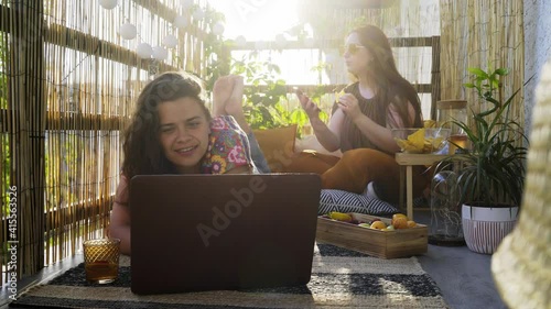 joyful women use modern laptop and drink delicious natural cocktails spending time together on light decorated terrace on sunny summer day photo