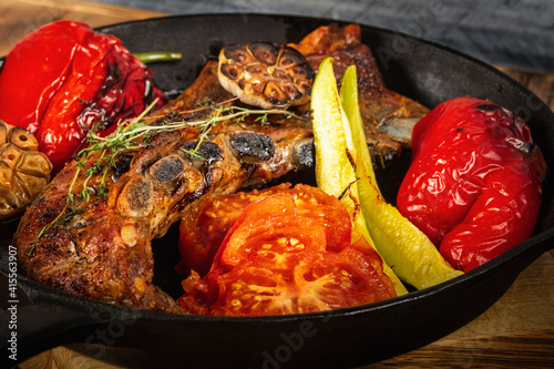  Pork ribs and vegetables on a cast iron pan. Wooden background. Close up. Selective focus.