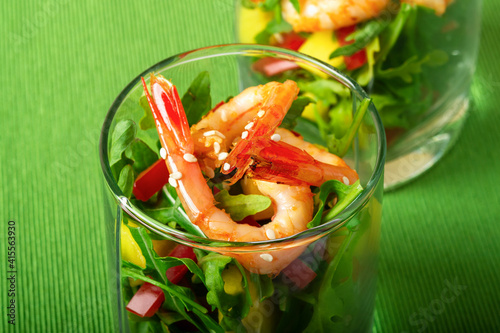 A salad of mango, sweet pepper, rukkola and garlic-fried shrimp in a glass. Close up. Selective focus. Green background.