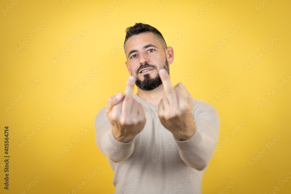 Handsome man with beard wearing sweater over yellow background showing middle finger doing fuck you bad expression, provocation and rude attitude. screaming excited Handsome man with beard wearing sweater over yellow background showing middle finger doing fuck you bad expression, provocation and rude attitude. screaming excited
