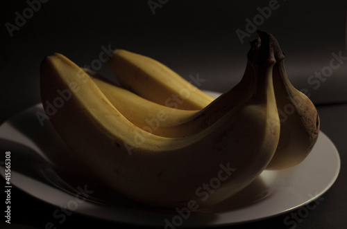 Foto archivo de  3 Plátanos amarillos y un plato blanco con un fondo oscuro en clave baja (Low Key) photo