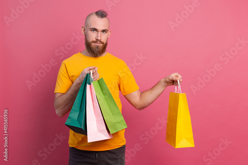 Happy bearded positive man casual look with colorful shopping bags studio pink background