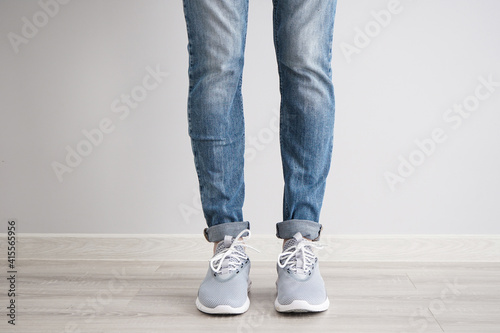 Legs of a young man in jeans and sneakers on a gray background.