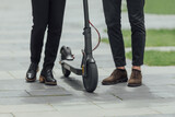 Legs of a man and woman in stylish outfit stand on electric scooter on the street