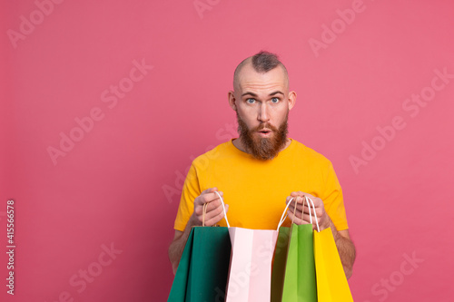 Happy bearded positive man casual look with colorful shopping bags studio pink background