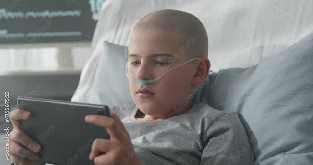 Sick kid with nasal oxygen tube in hospital bed using digital tablet