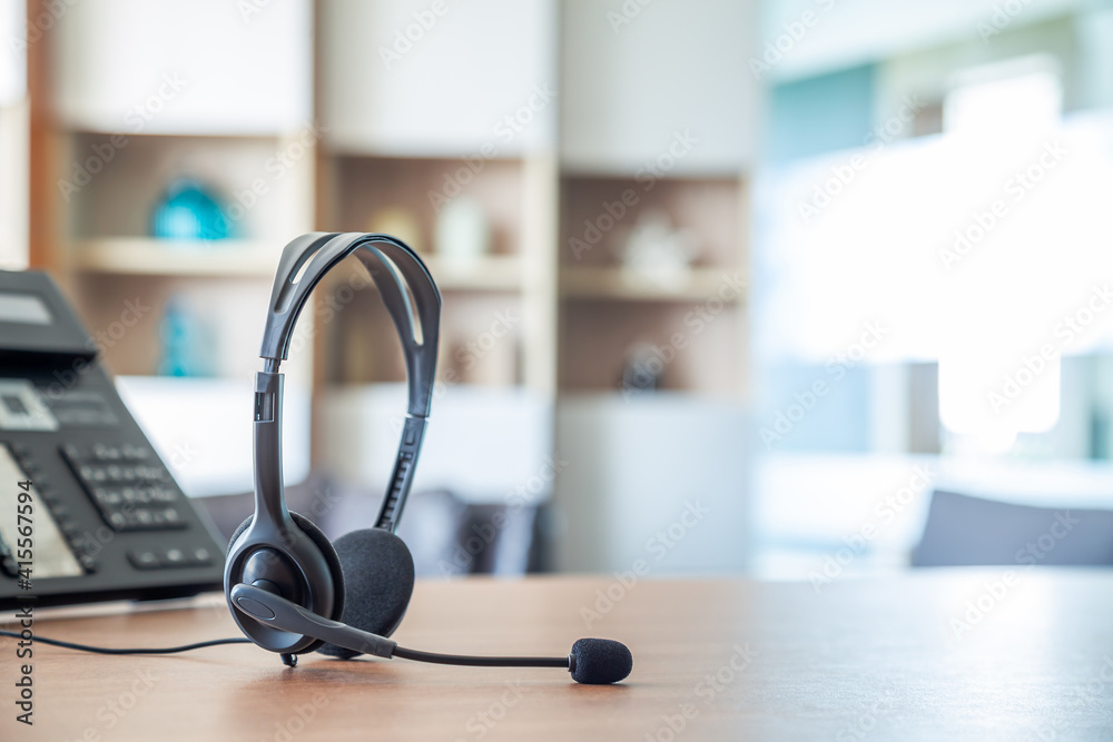 Obraz premium Close up soft focus on headset with telephone devices at office desk for customer service support.VOIP headset for customer service support (call center) concept.