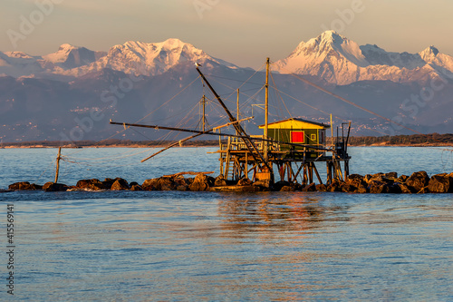 Trebuchet fishing hut at sunset against the Alps covered with snow, Marina di Pisa, Tuscany, Italy photo