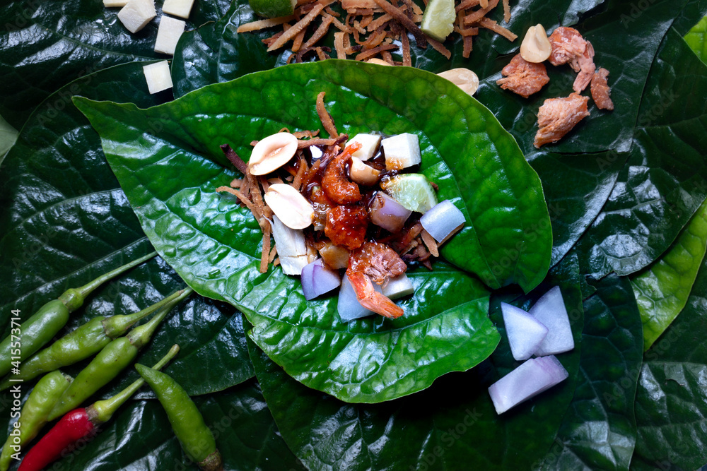 Miang Kham Small pieces of garnish are arranged on basil leaves. Contains ginger, lime, roasted coconut, onions, dried shrimp and peanut lad. Was placed on the basil leaves.