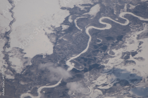 from the window of the plane you can see the mountains of the far eastern region of russia, day, snowy. clouds are visible above the ground