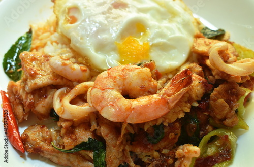 spicy stir fried shrimp and squid curry eat couple with rice topping egg on plate