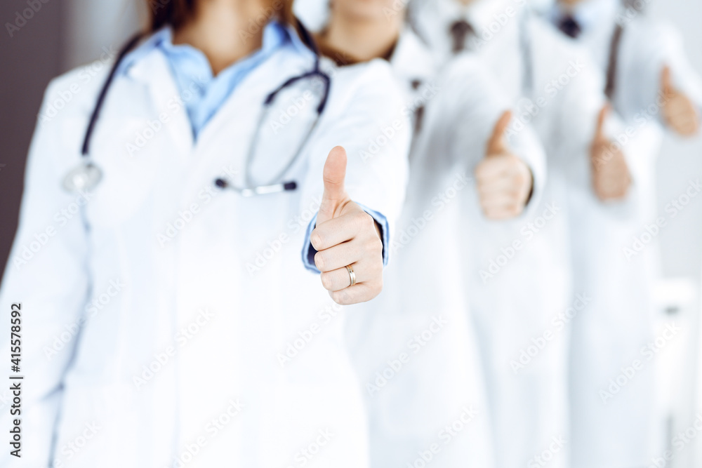 Group of modern doctors standing as a team with thumbs up in hospital office. Medical help, insurance in health care, best desease treatment and medicine concept Group of modern doctors standing as a team with thumbs up in hospital office. Medical help, insurance in health care, best desease treatment and medicine concept