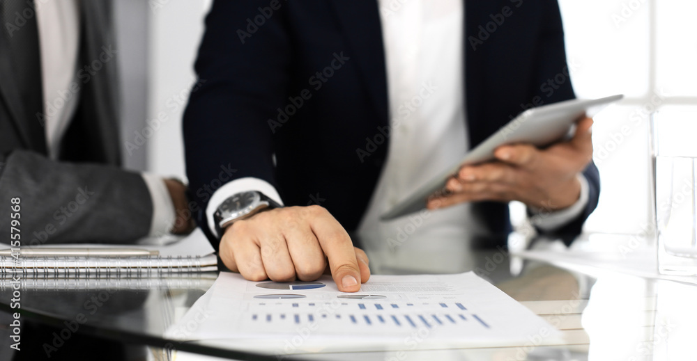 Business people using tablet computer while working together in modern office. Unknown businessman sitting at the desk with his colleague or partner. Teamwork and partnership concept Business people using tablet computer while working together in modern office. Unknown businessman sitting at the desk with his colleague or partner. Teamwork and partnership concept