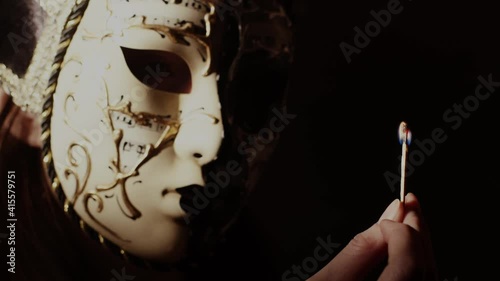 Mysterious lady in carnival mask lighting a match. Lady death on a black background. Isolated, dark person in a theatrical costume.